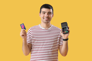 Wall Mural - Young man with payment terminal and credit card on yellow background