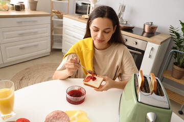 Canvas Print - Young beautiful happy woman making tasty toast with jam in kitchen