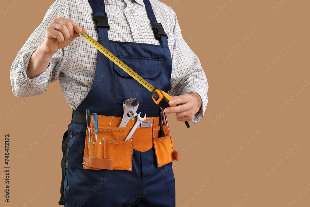 Male construction worker with measuring tape and tools on brown background