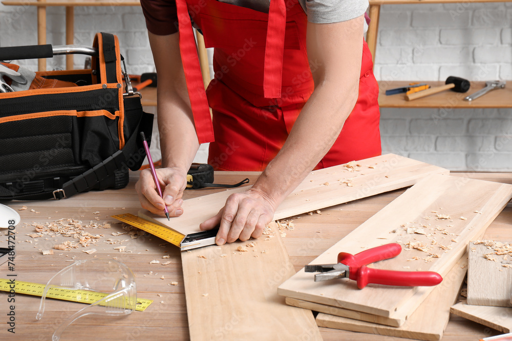 Male carpenter measuring wooden plank with square ruler in workshop