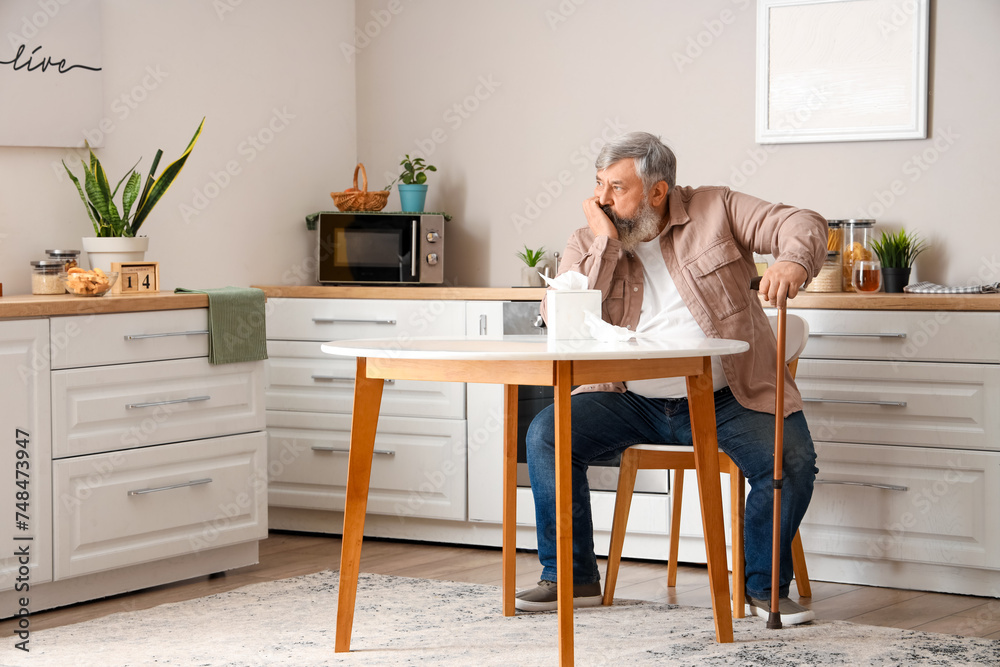 Portrait of sad senior man with tissues sitting at table in kitchen