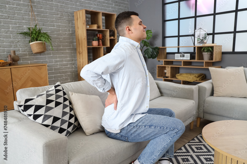 Young man suffering from back pain on sofa at home