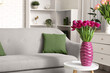 © Pixel-Shot - Vase with fresh tulips on table near sofa in living room