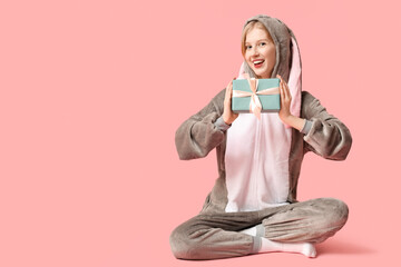 Wall Mural - Beautiful young happy woman in bunny costume with gift box sitting on pink background. Easter celebration