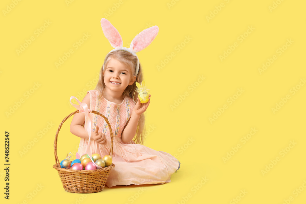 Little girl in bunny ears with Easter eggs sitting on yellow background