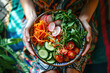 Hands hold a bowl with a variety of colorful chopped vegetables. Healthy raw food with nuts and vegetables. View from above.