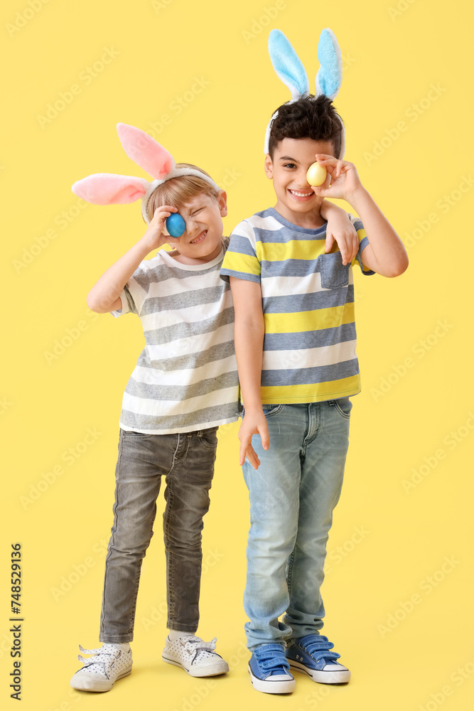 Cute little boys in bunny ears with Easter eggs on yellow background