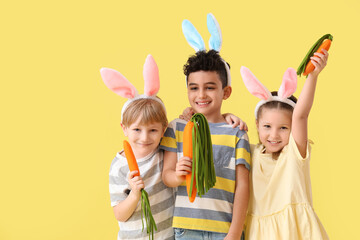 Wall Mural - Cute little children in bunny ears with toys carrots on yellow background. Easter celebration