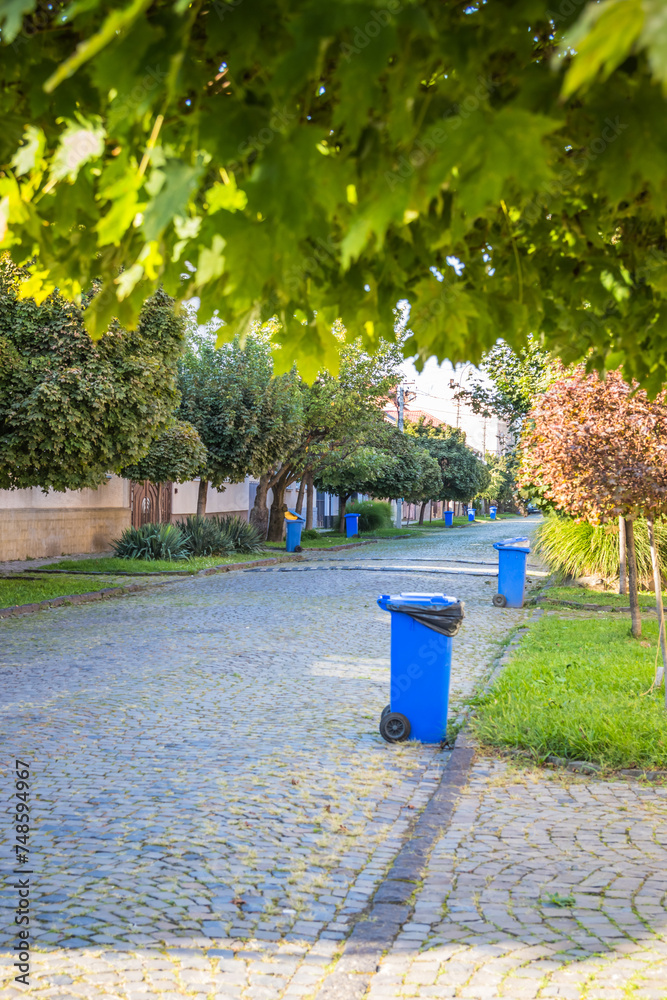 Blue garbage cans on the street in a small town near every house. Centralized garbage collection in a small cozy European city. Garbage collection on a certain day of the week.