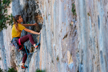 Wall Mural - The girl climbs the rock. The climber trains on natural terrain. Extreme sport.  A woman overcomes a difficult route rock climbing..