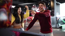 Multiracial Couple Of Friends Playing Pinball In Arcade Game Room Celebrating Victory In The Game With Jumping And Hugging