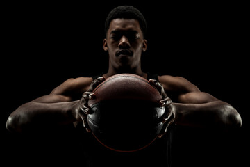 Wall Mural - Basketball player holding a ball against black background. Serious concentrated african american man.