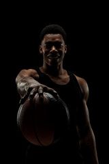 Wall Mural - Basketball player holding a ball against black background. Serious concentrated african american man.