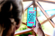 Summer sale offer Ad. Up to 50% off. Woman holding a mobile phone showing an offer or coupon on the screen.