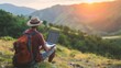 Young man freelancer traveler wearing hat anywhere working online using laptop and enjoying mountains view