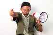 Indonesian Muslim man in koko and peci gives a thumbs-down gesture while holding a megaphone, expressing disapproval or dissatisfaction. Isolated on a white background
