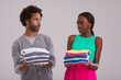 © peopleimages.com - People, studio and pile of laundry in hand for neat, cleaning day or washing clothes together. Couple, surprise and shocked for organised wardrobe with color choice, fashion or ocd on grey background