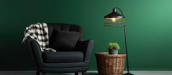 A black armchair with a basket filled with a cushion plaid sits next to a lamp in a living room with a green wall. The cozy setup invites relaxation and comfort.