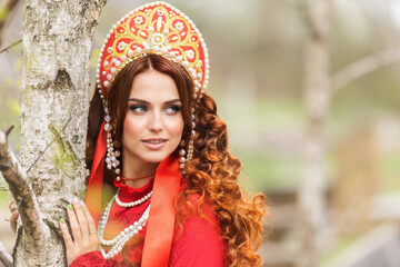 russian girl in traditional russian sarafan and kokoshnik embroidering outdoors