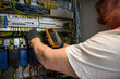 © juraj - an electrician in a cap, yellow glasses and an orange vest measures electric current with a digital multimeter on a distribution box