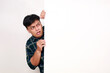 © ArvStd - Portrait of young asian man standing behind an empty signboard with afraid face expression