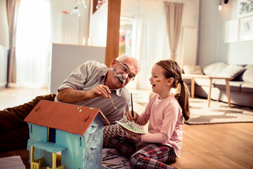 Grandfather and granddaughter painting a toy house together at home