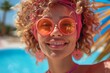 A joyous young woman with curly hair and trendy sunglasses enjoying a sunny day by the pool, smiling brightly