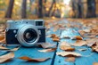 A classic vintage camera lays amongst vibrant autumn leaves on a wooden board, capturing the essence of fall