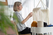 Middle-aged woman knits lampshade for interior using macrame technique. Woman knits boho chandelier at home
