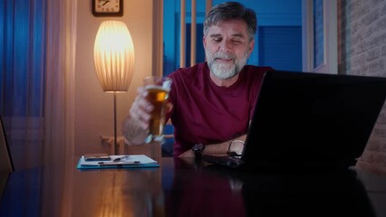 Wall Mural - Freelancer working at home drinking beer, night time. Positive thoughtful male employee pondering considering idea looking at computer screen making decision. Living room, working on laptop computer.