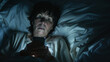 elderly woman lying in bed at night, looking at her smartphone with a concerned or possibly startled expression.