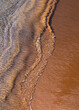 Ocean surf on sandy beach, top view. Nature background with red sand and waved lines of seawater on a sand shoreline.