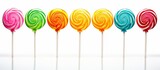 Fototapeta Tęcza - A close-up view of a row of colorful lollipops stacked on top of each other, showcasing a variety of vibrant colors such as red, blue, yellow, and green. The lollipops are isolated on a white
