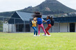 Three biracial girls are playing on a grassy field in school, with a mountain in the background