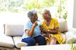 Senior African American woman and senior biracial woman share a moment over a cup of tea at home
