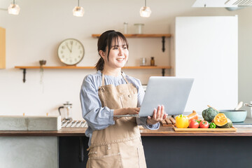 Sticker - 家のキッチンでノートパソコンを使ってレシピや栄養素を検索するアジア人女性
