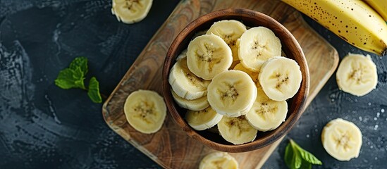 Sticker - A wooden bowl filled with freshly sliced bananas sits atop a wooden chopping board. The golden bananas are neatly arranged, ready to be enjoyed as a healthy snack or ingredient in a recipe.