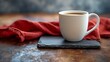 A white coffee mug on a piece of gray slate with a red linen cloth napkin behind it. 