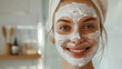 A satisfied woman applied a face mask and is waiting for the result in the bathroom at home. The girl smiles and uses daily multi-step facial skin care