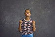 © Studio Romantic - Portrait of happy emotional african american woman rejoicing in her victory standing on gray background. Excited and joyful woman sincerely laughing and rejoicing with clenched fists. Concept of luck.