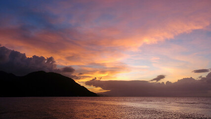 Wall Mural - Sunset over a tropical island. Clouds over a tropical island in the rays of the setting sun. Sunset background.