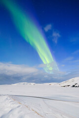 Wall Mural - Aurora Borealis in Iceland. Northern Lights over snow field. A winter night landscape with bright lights in the sky. Landscape in the north in winter time. A popular place to travel.