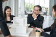 © Bavorndej - Group of business professionals gathers around a table, engaging in lively discussion while examining a detailed building model.
