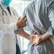 © Krystian - Doctor is diagnosing a patient's back pain in a hospital examination room. A male with back pain sees a doctor for treatment
