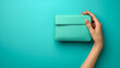 Female hand holding a turquoise clutch on a blue background with  copy space. generative ai