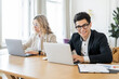 © muse studio - Smiling professionals working on laptops in a bright, modern office space.