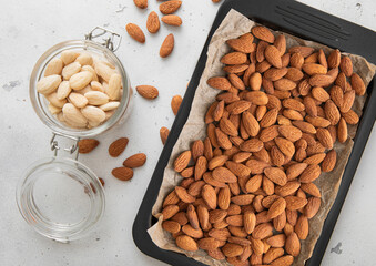 Wall Mural - Tray with raw healthy whole almond nuts and peeled nuts in jar on light kitchen background.Macro.