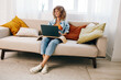 © SHOTPRIME STUDIO - Smiling woman using laptop in cozy living room
