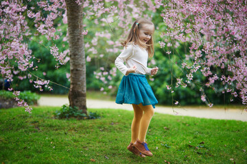 Wall Mural - Adorable preschooler girl enjoying nice spring day in park during cherry blossom season