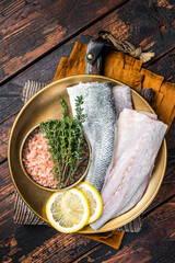 Wall Mural - Uncooked Raw Sea Bass fillets, Seabass fish with thyme, pink salt and lemon. Dark background. Top view